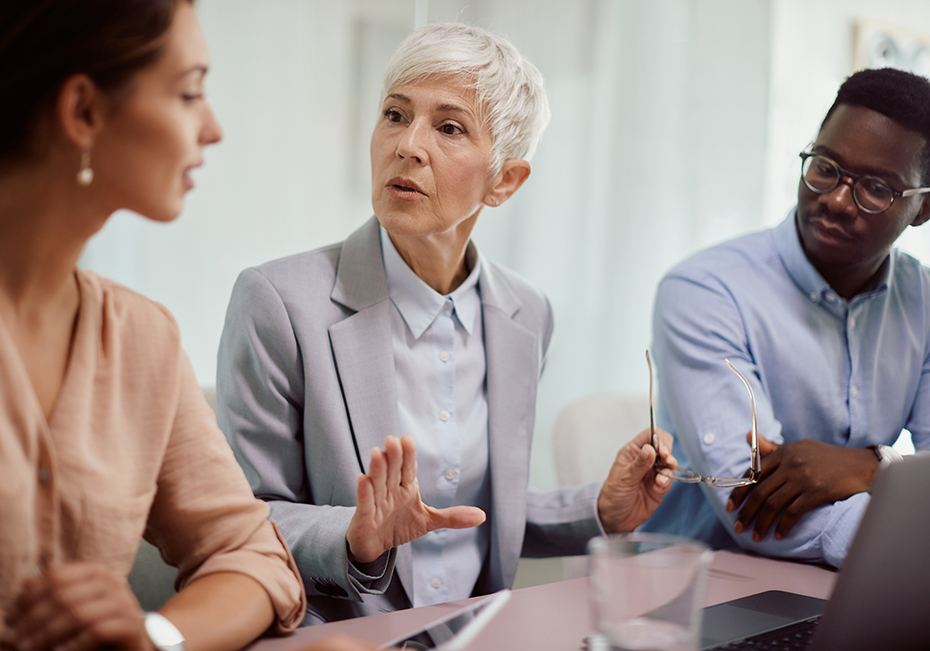 A senior leader in conversation with two younger colleagues at a meeting table, illustrating the LIFT UP Professional Development Series now delivered through Loxis